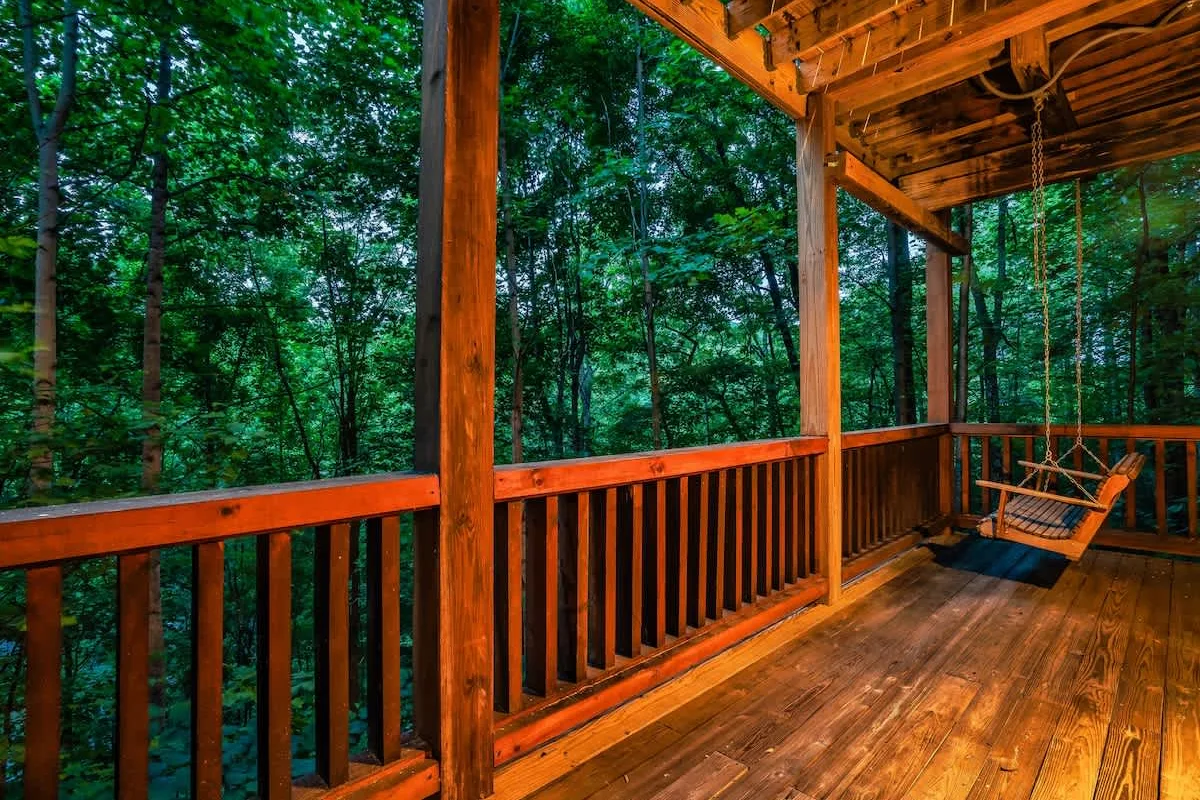 Covered deck at Break Point Lodge with a porch swing looking into the trees